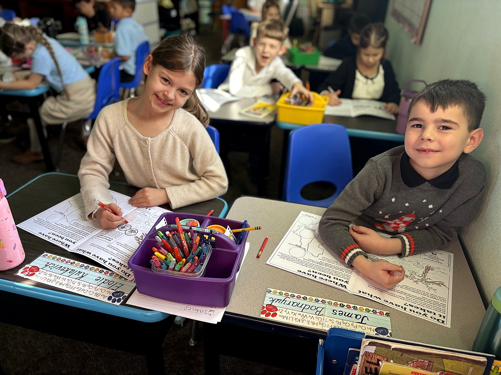Two young students smiling at their desks in a small classroom