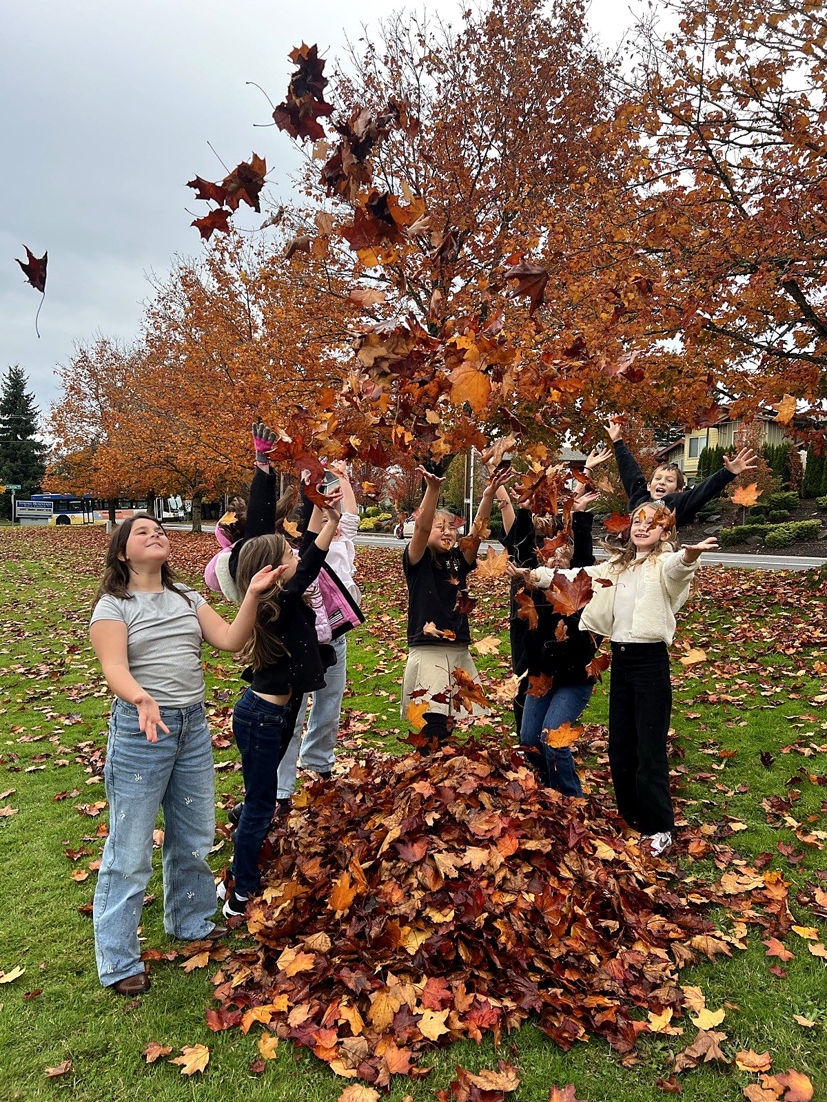 Young students laughing as they throw autumn leaves outdoors