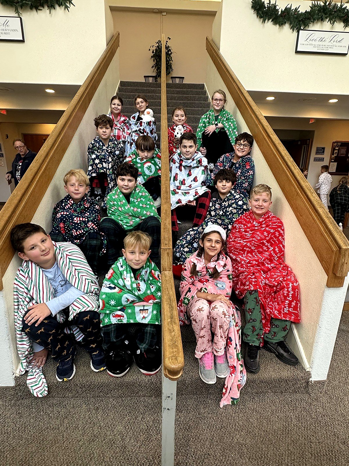 A large group of students in Christmas pajamas posing together on the stairs