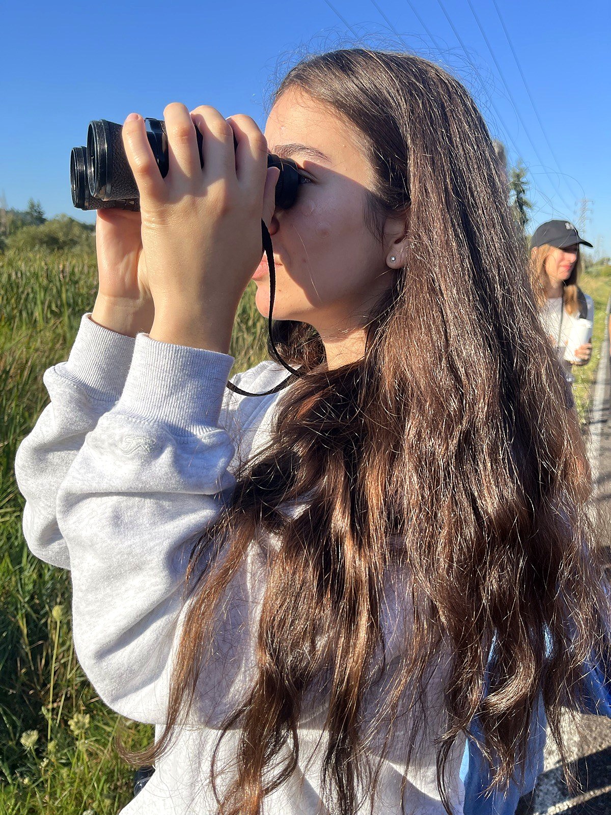 A high school student using binoculars on an outdoor science field study