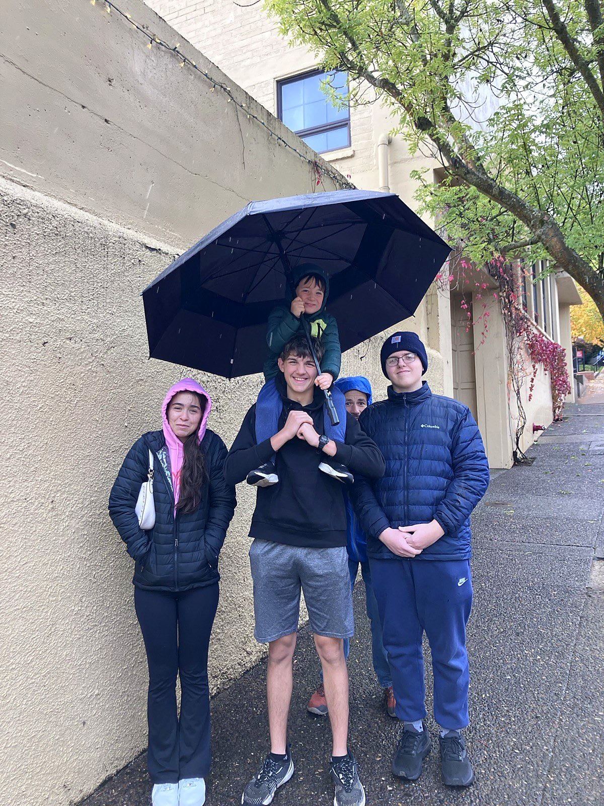 High school students laughing together under an umbrella on a rainy field trip